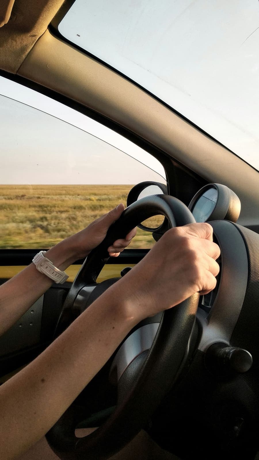 Hände am Lenkrad während der Fahrt durch weite Landschaft