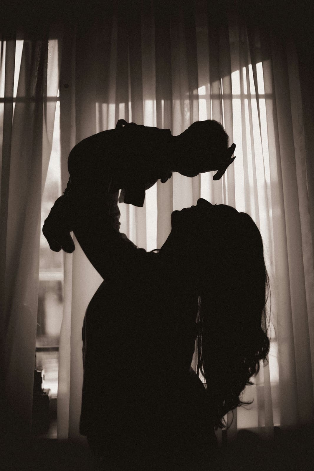 Silhouette: Mutter hebt ihr Baby vor einem Fenster hoch