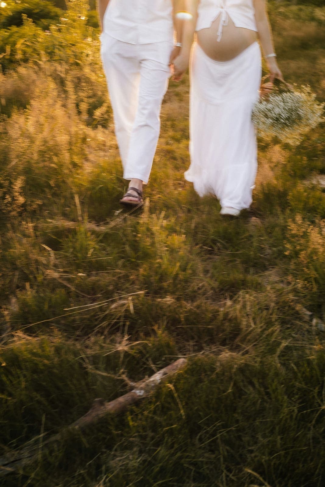 Schwangere und ihr Partner gehen Hand in Hand durch ein Feld im Abendlicht